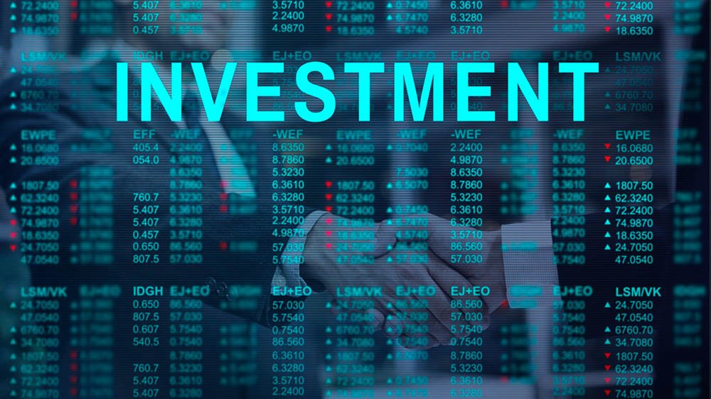 “Digital display of stock market data showing various stock symbols, prices, and directional arrows. The word ‘INVESTMENT’ appears in large, bold, cyan letters across the screen. In the background, two individuals are faintly visible shaking hands, symbolizing a business agreement.”