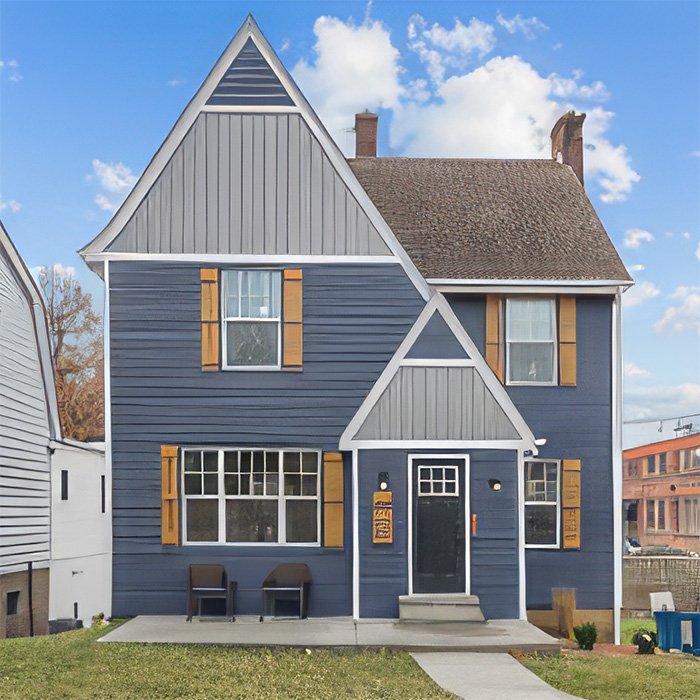 A two‑story house with dark blue siding, white trim, and wooden shutters stands under a partly cloudy sky. The front door sits beneath a small porch with two steps, and two chairs are placed near a large front window. Neighboring buildings are visible on both sides.